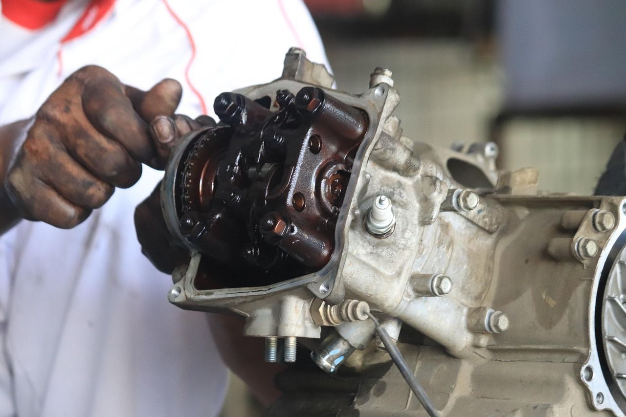 Mechanic working on an engine, with hands in view. The engine is open, with visible components and oil residue.