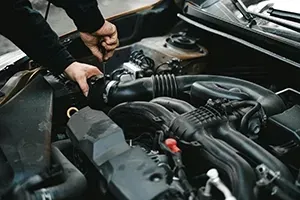 Hands working on a car engine, unscrewing a black component inside the open hood.