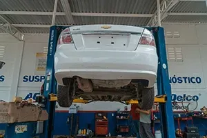 White car on a hydraulic lift in a garage, undercarriage visible.