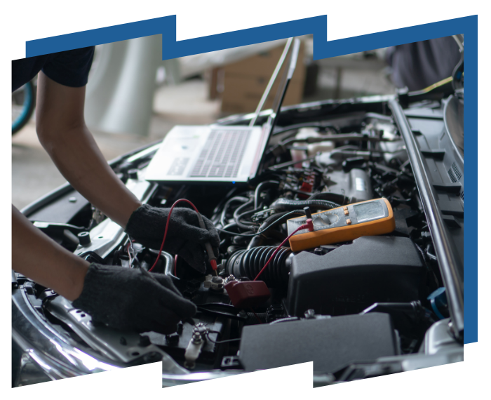 A man is working on a car with a laptop and a multimeter.
