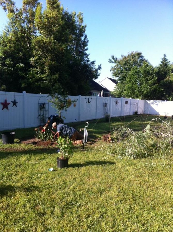 a man is working in a garden in front of a white fence
