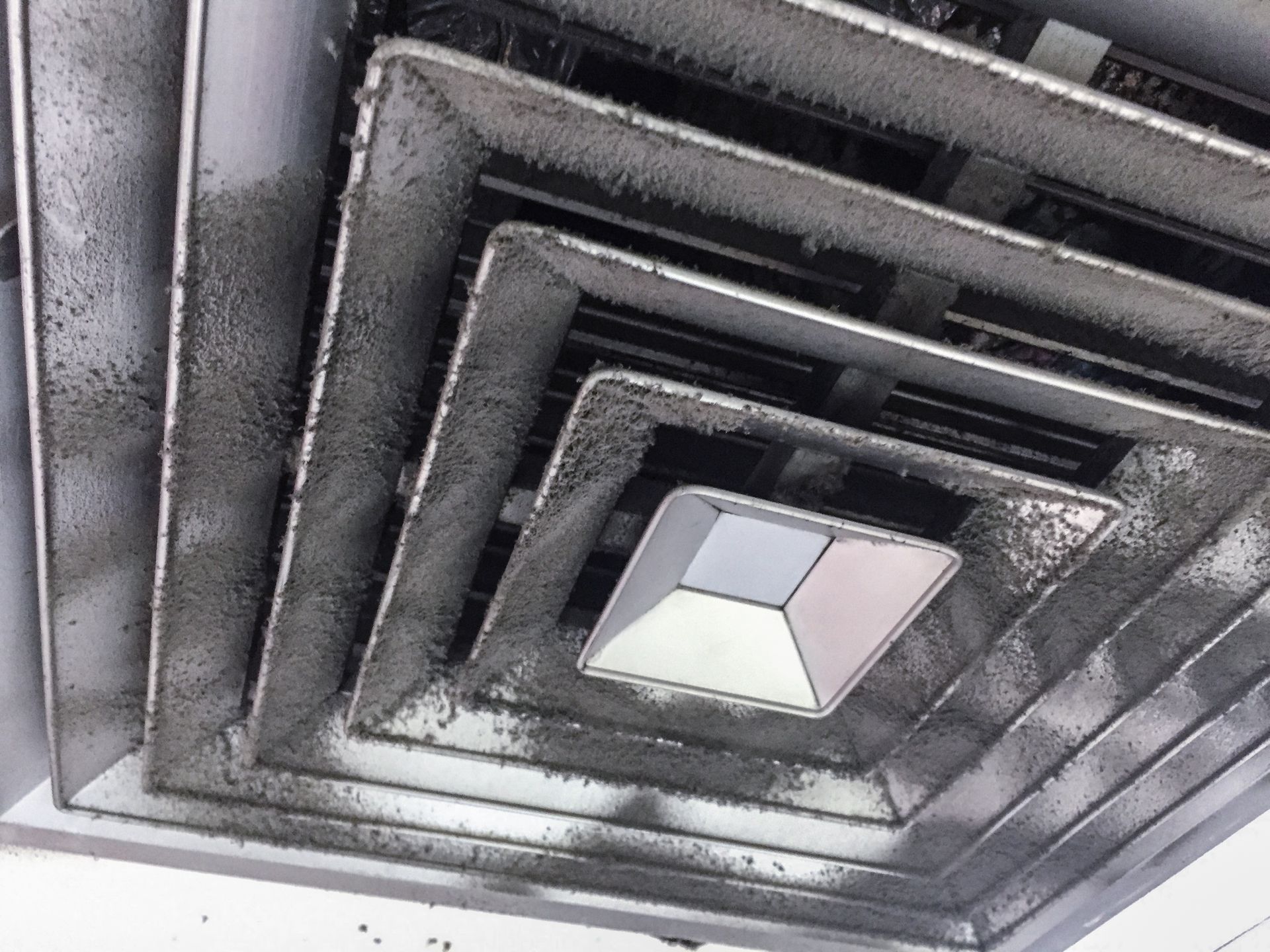 A dirty square ceiling air vent covered in thick layers of dark dust and debris.