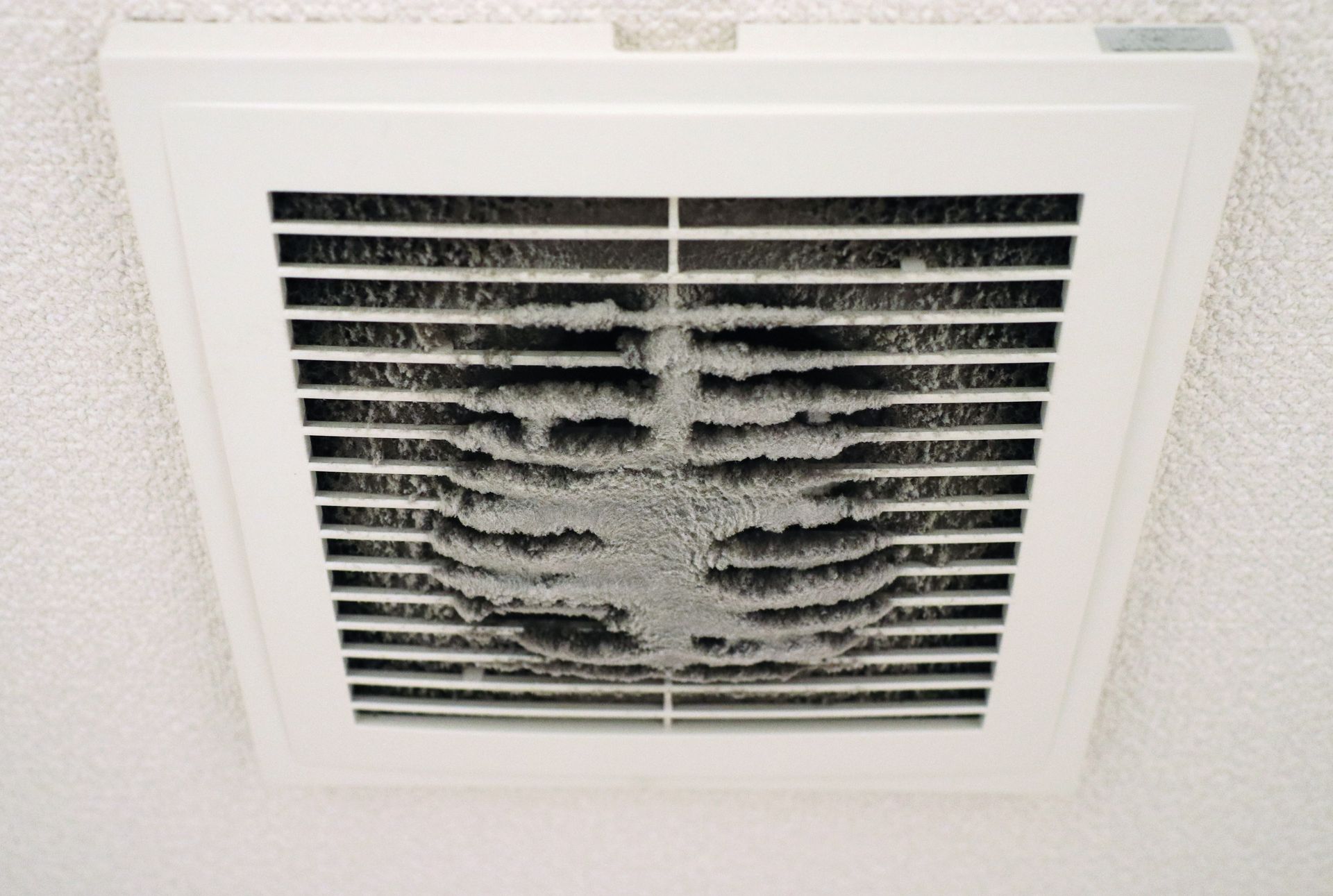A square white bathroom ceiling exhaust fan grill clogged with a significant buildup of grey dust and lint.