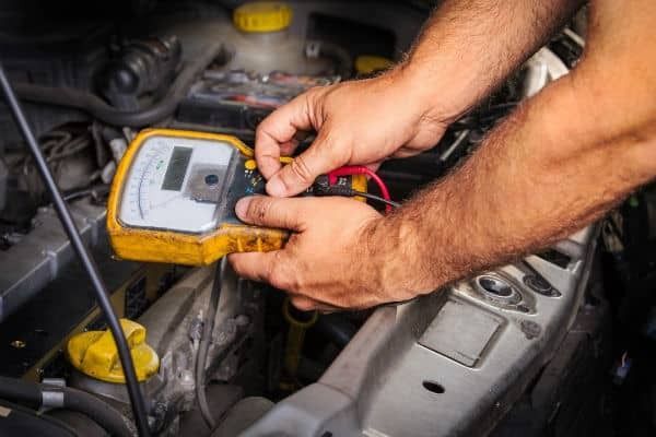 A man is working on a car battery with a multimeter.
