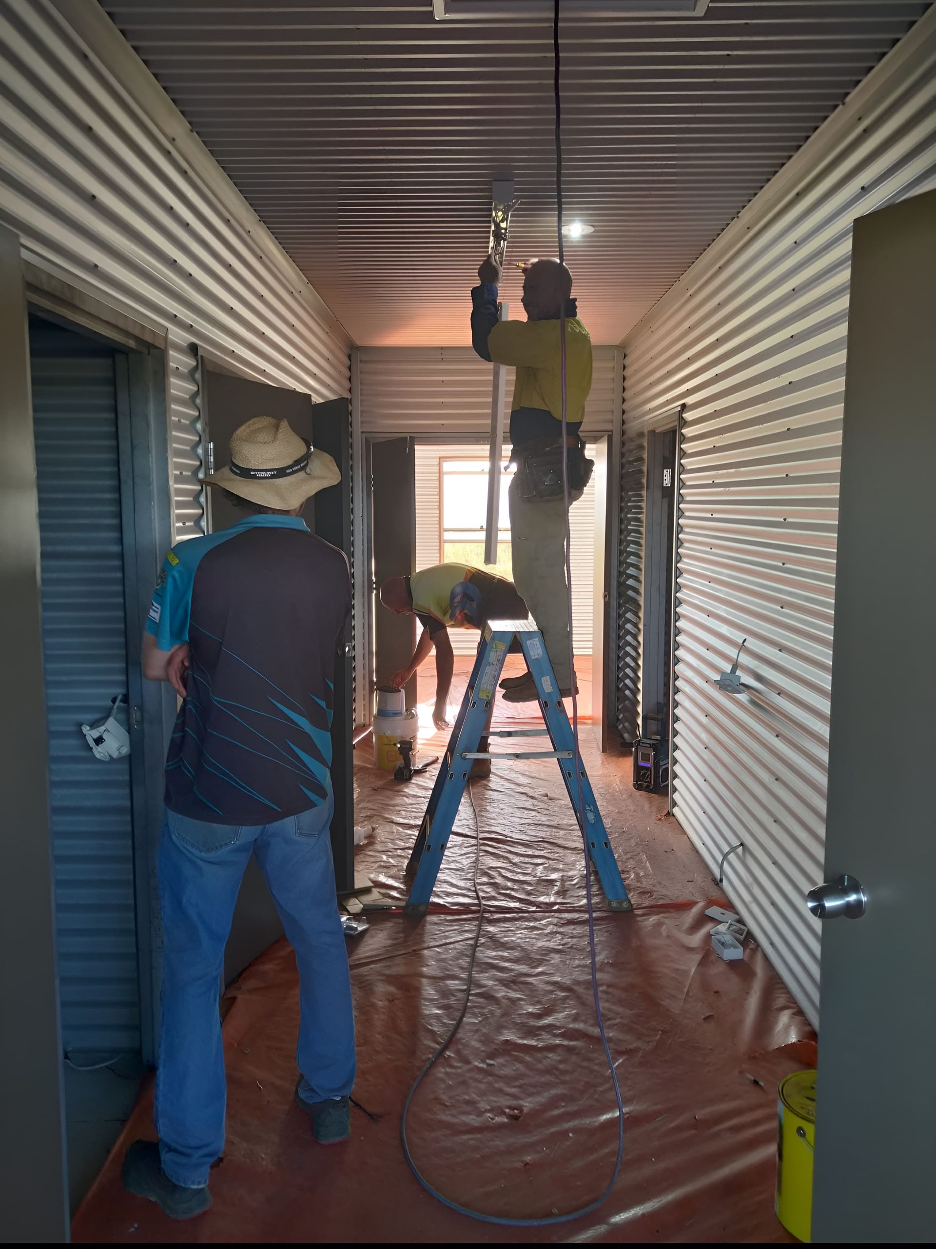 Two men a working in a hallway with another man standing on a ladder fixing a light — Alice Springs Electrical Services In Araluen, NT