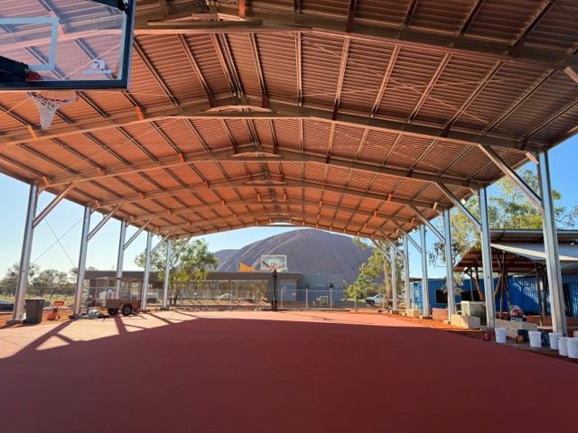 An outdoor basketball court with metal roof and Uluru in the background — Alice Springs Electrical Services In Araluen, NT