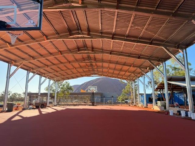An outdoor basketball court with metal roof and Uluru behind — Alice Springs Electrical Services In Araluen, NT