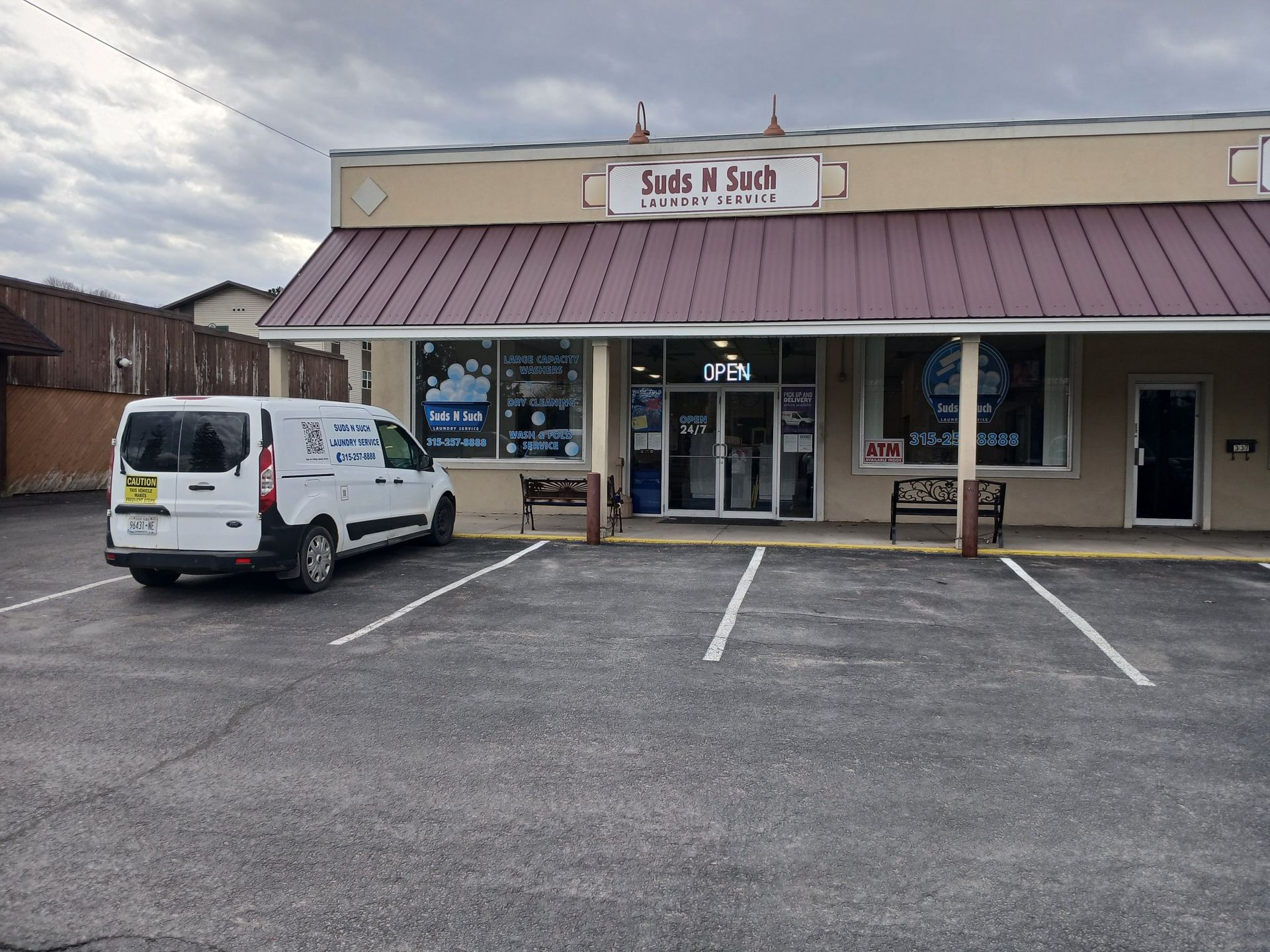 A white service van parked in front of a beige commercial building with a maroon metal awning and a 