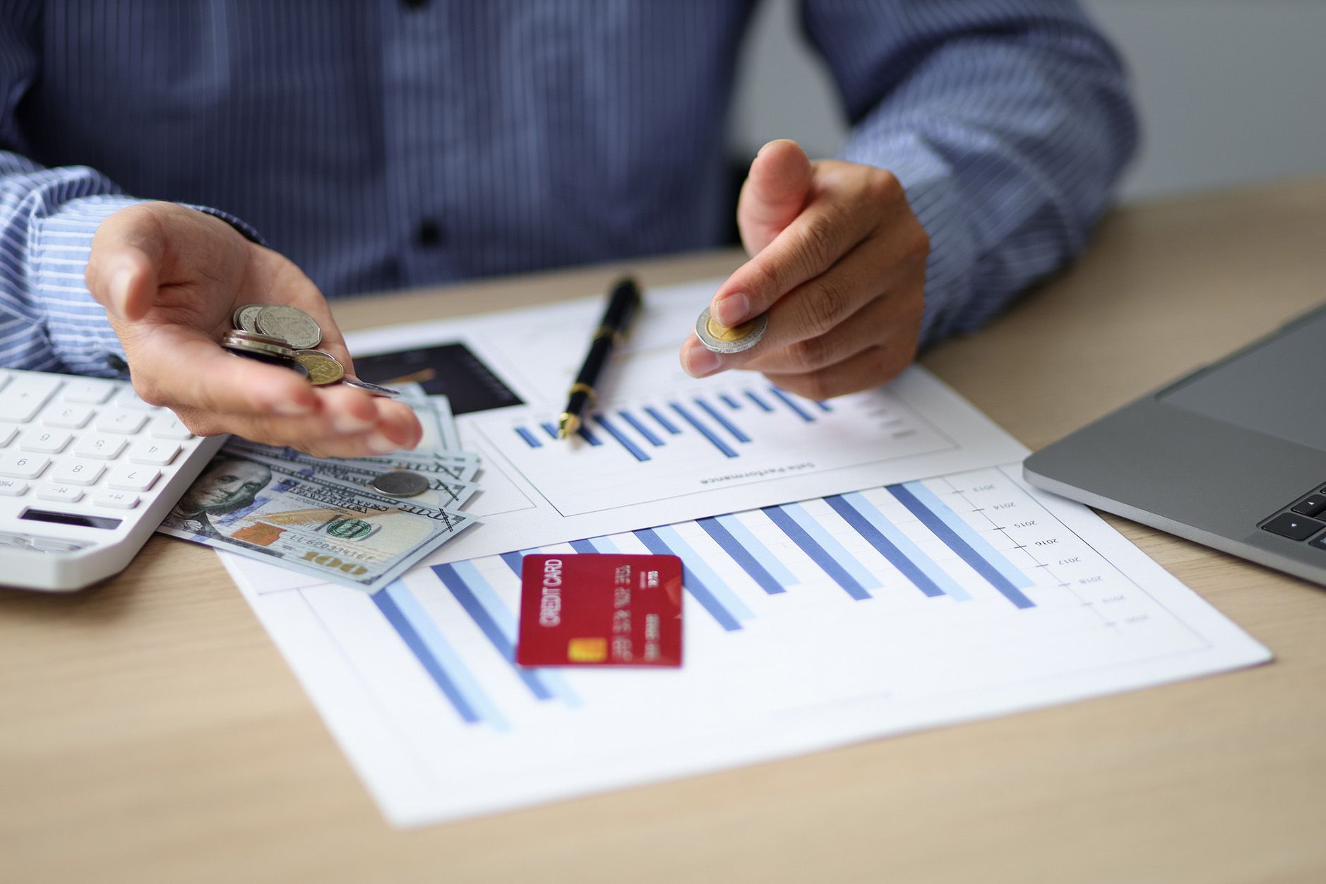 Person with cash, coins, and credit card on financial documents next to a laptop and keyboard.