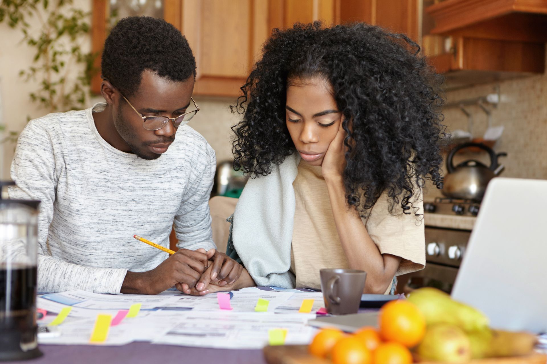 Couple reviewing financial documents at a kitchen counter. They appear focused and possibly stressed.