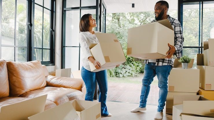 Couple carrying moving boxes into a bright, modern living room.