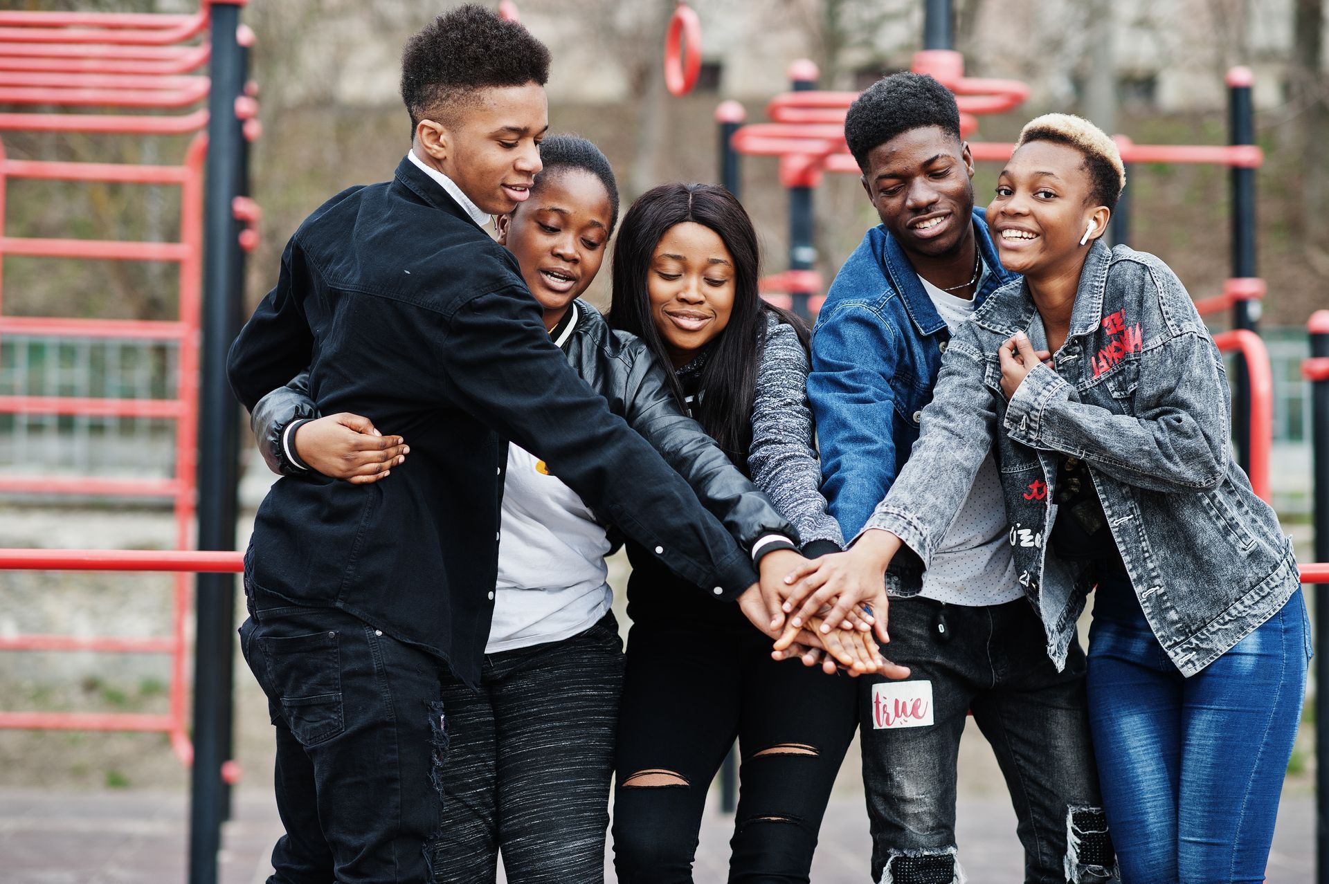 Group of friends with hands together, smiling, at a playground.