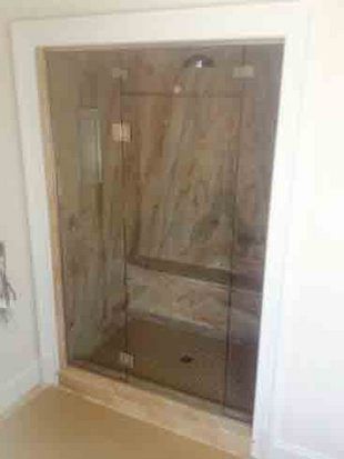 Glass shower enclosure with beige marble walls and white trim.