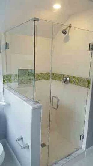 Glass shower stall with a chrome handle and showerhead, green tile accent, and light fixtures.