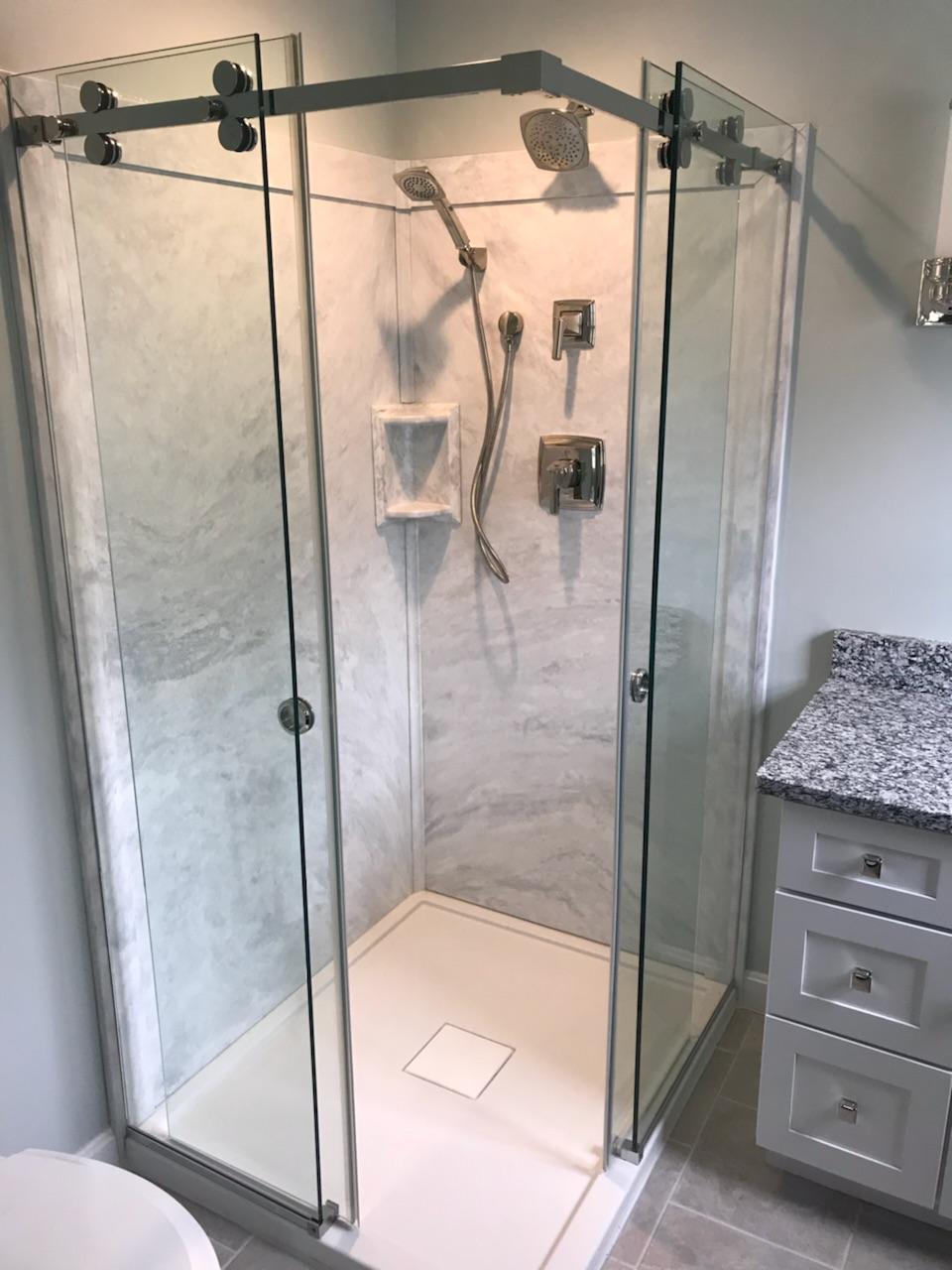 Glass shower enclosure with sliding door, marble-like wall, and white base in a modern bathroom.