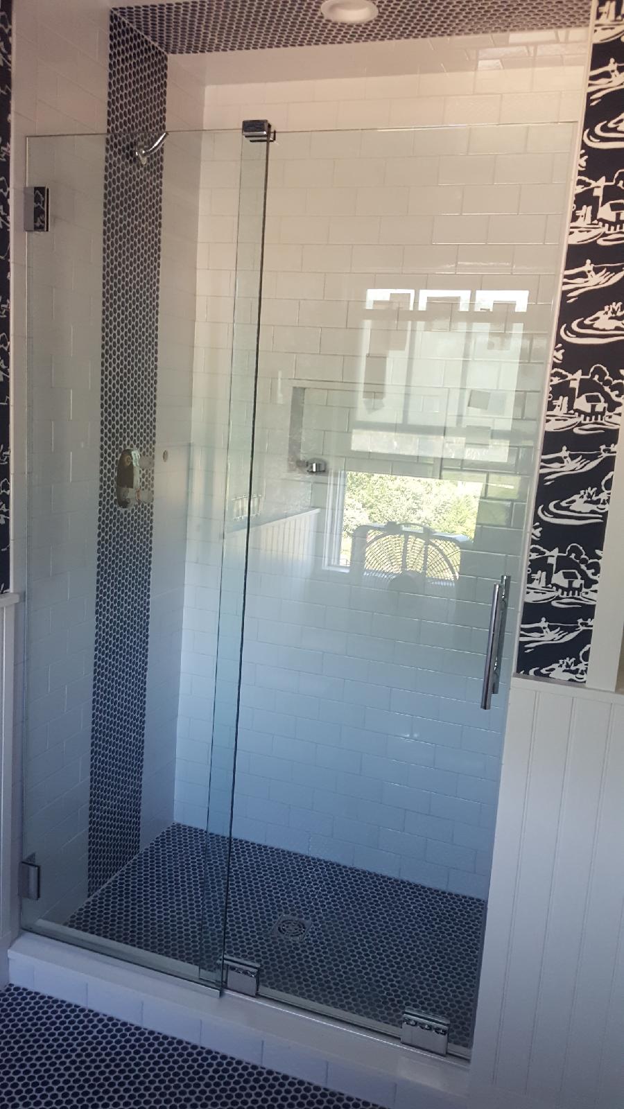 Glass shower with mosaic tiles, white subway tiles, and window reflection.