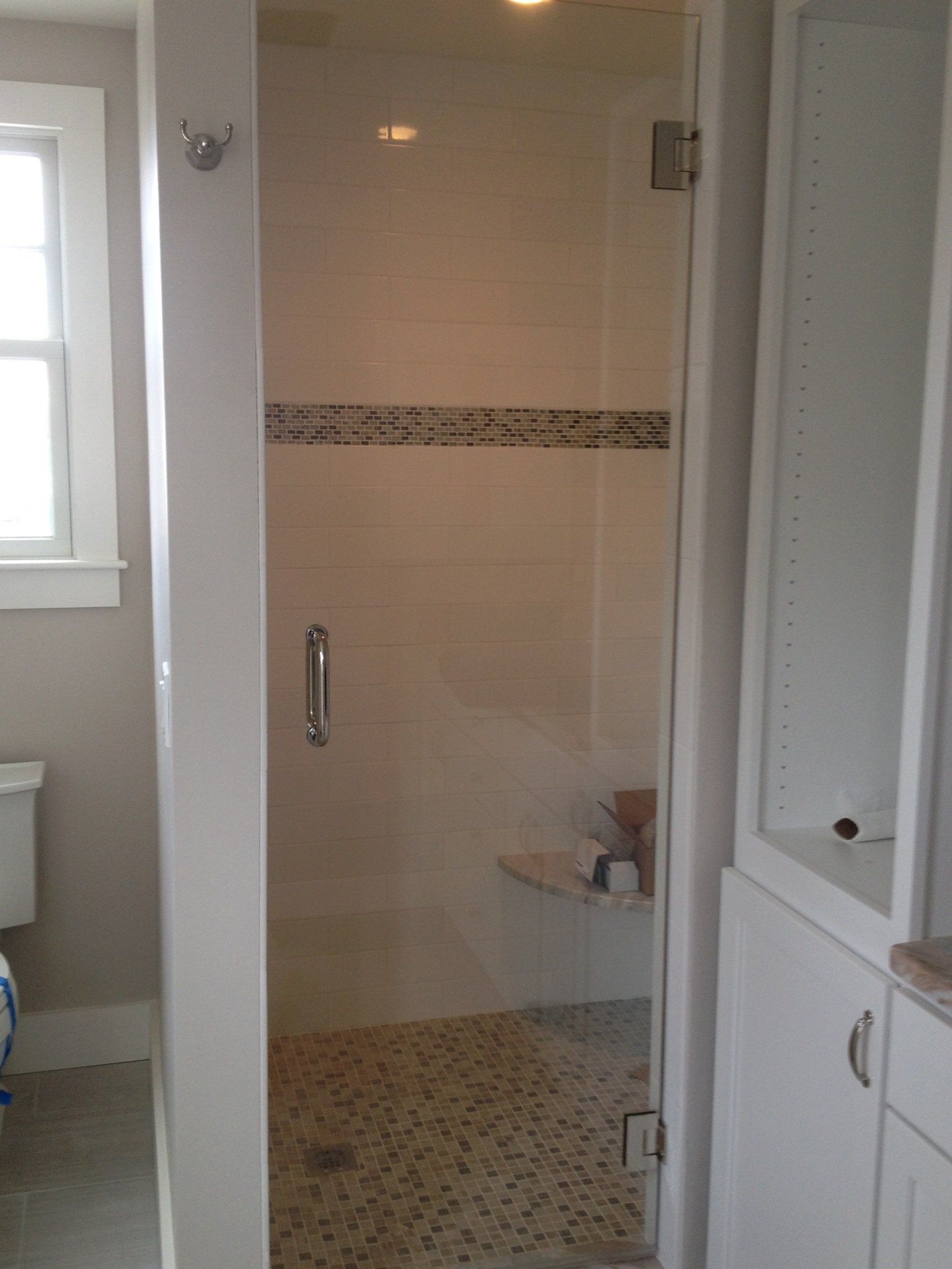 Shower stall with glass door, pebble floor, white tile, and built-in bench, in a white-walled bathroom.