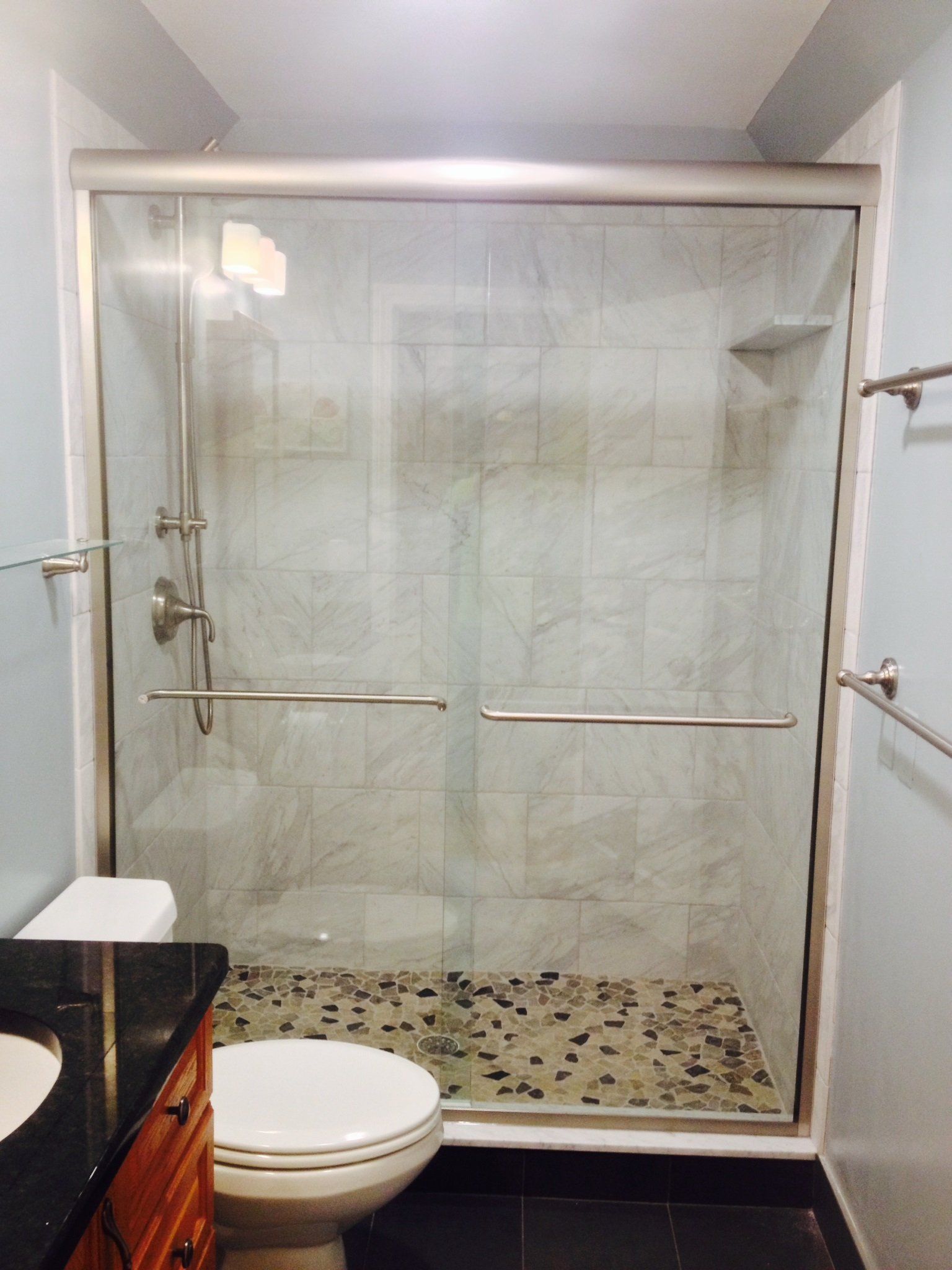 Shower with glass doors, stone floor, toilet, and vanity in a bathroom.