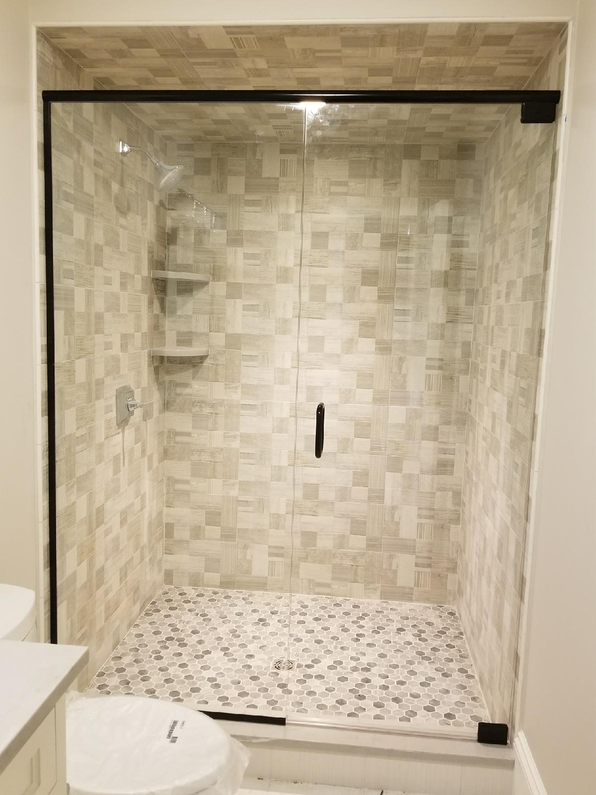 Shower with glass doors and black trim, tiled walls and floor.