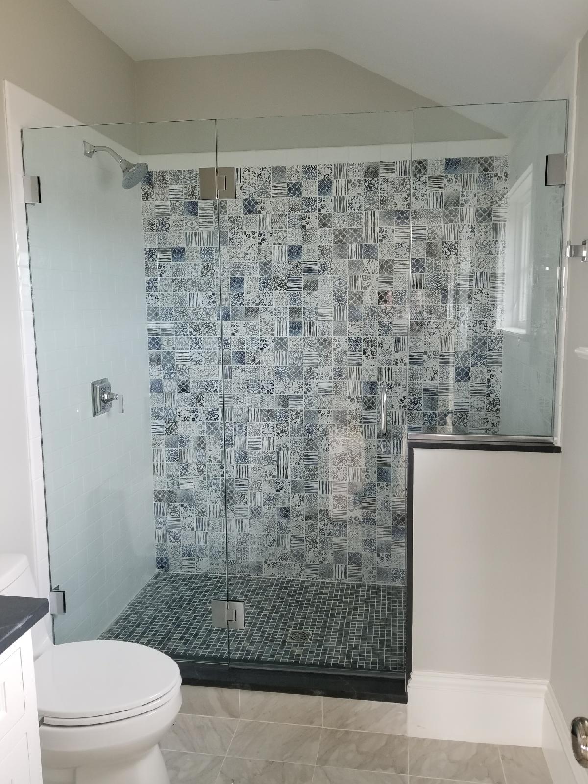 Glass shower with blue and white tile, black pebble floor, and a white toilet.