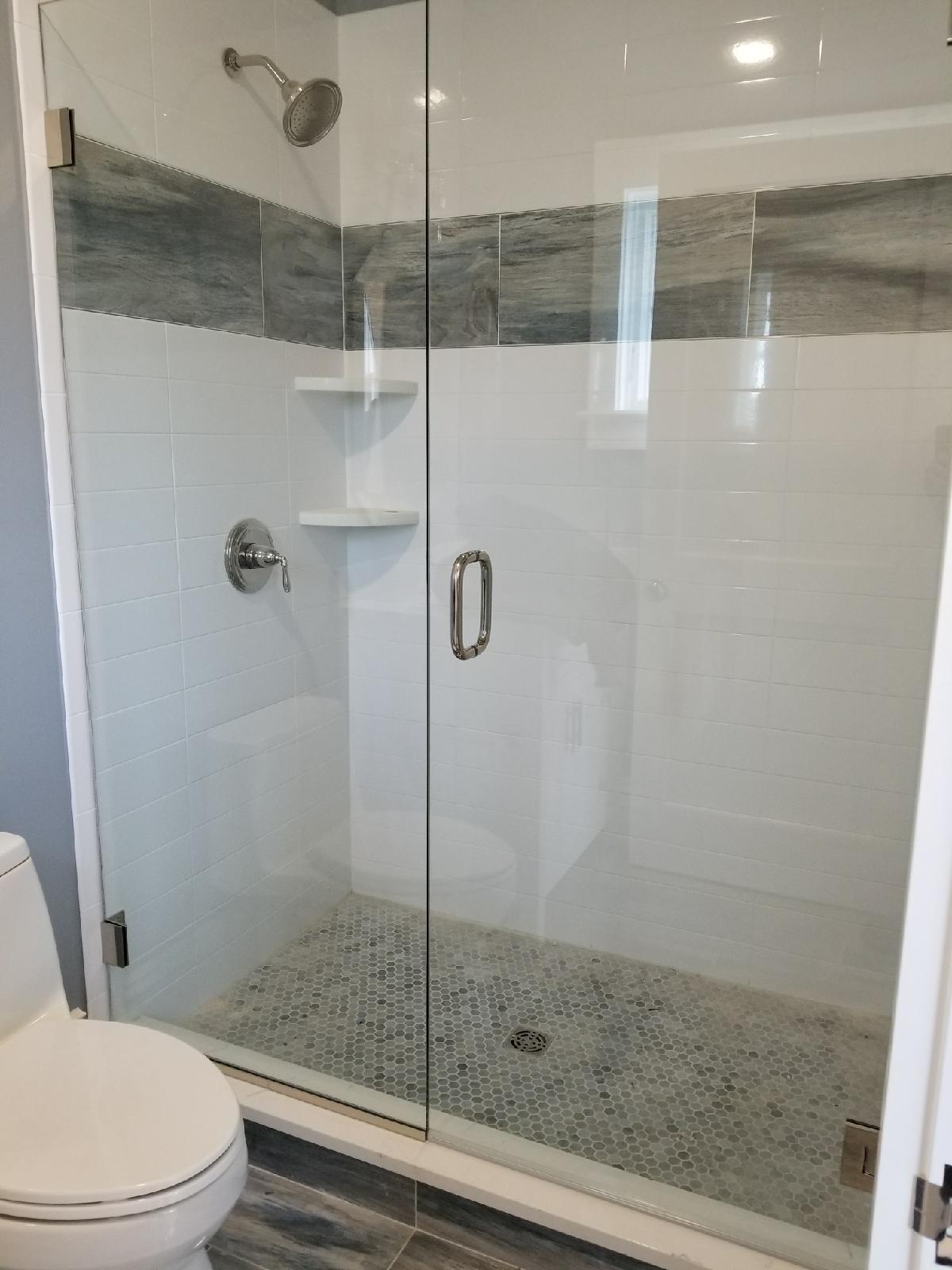 Shower with clear glass door, white tile walls, gray accent tile, and pebble floor.
