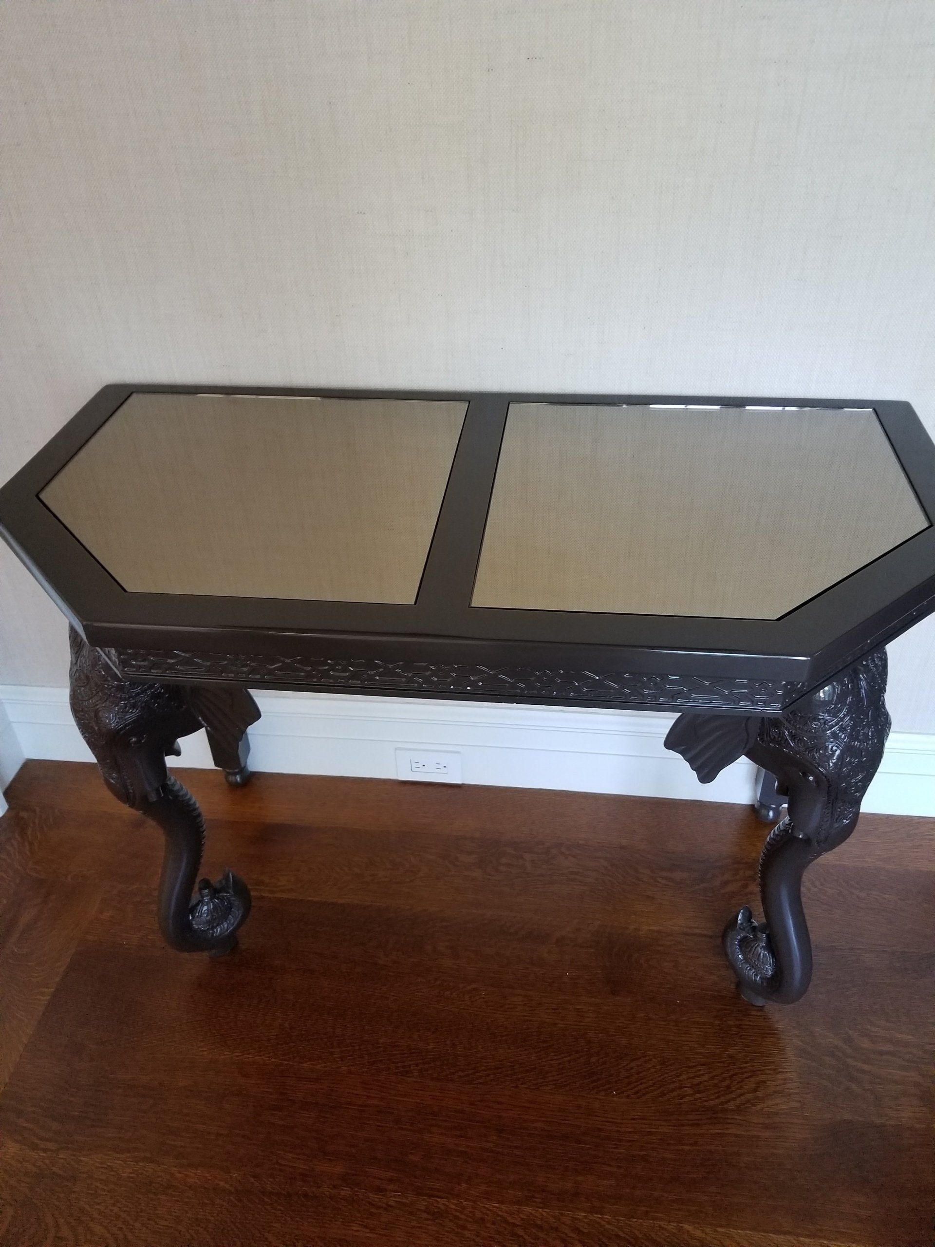 Dark wood, octagonal coffee table with mirrored top and carved legs on a hardwood floor.
