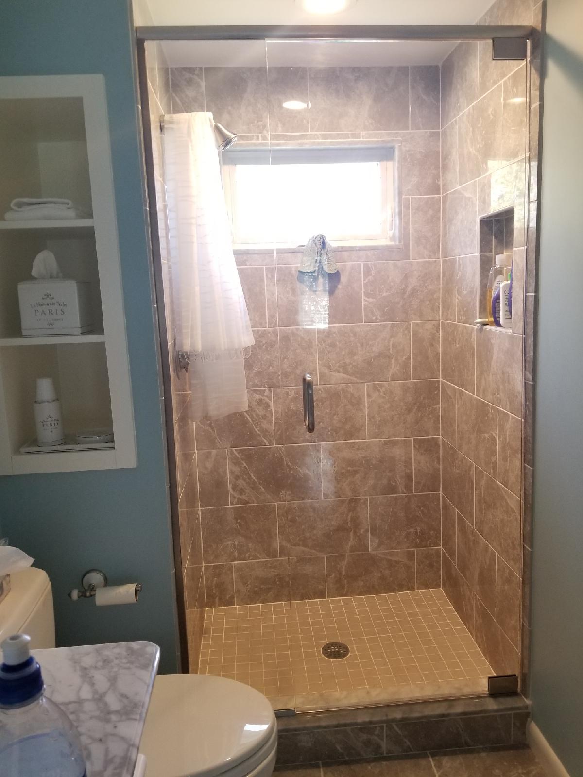 Shower with brown tiled walls and floor. Glass door and window. White shower curtain.