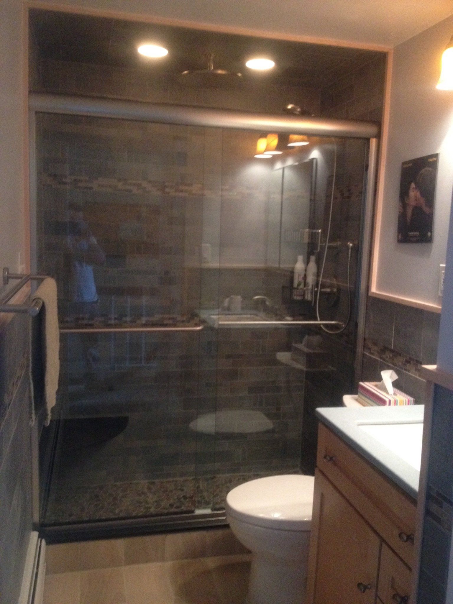 Bathroom with glass shower, toilet, and vanity. Dark tile walls, wood cabinet, and neutral color floor.