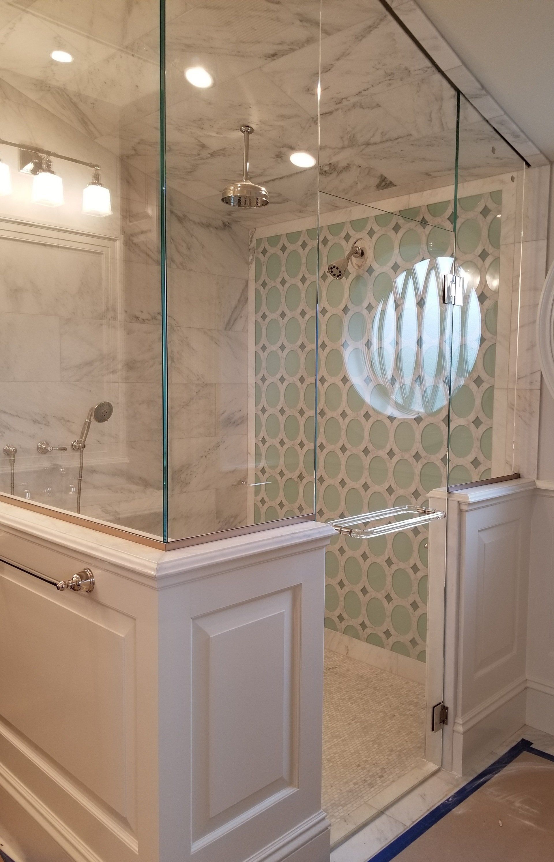 Shower with marble walls, glass enclosure, patterned tile accent, and white trim.