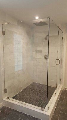 A glass shower enclosure with gray tiled floor and walls, chrome fixtures, and a recessed niche.