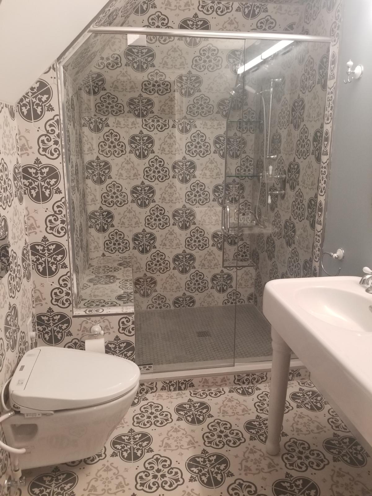 Bathroom with patterned gray and white tile, glass shower, toilet, and sink.