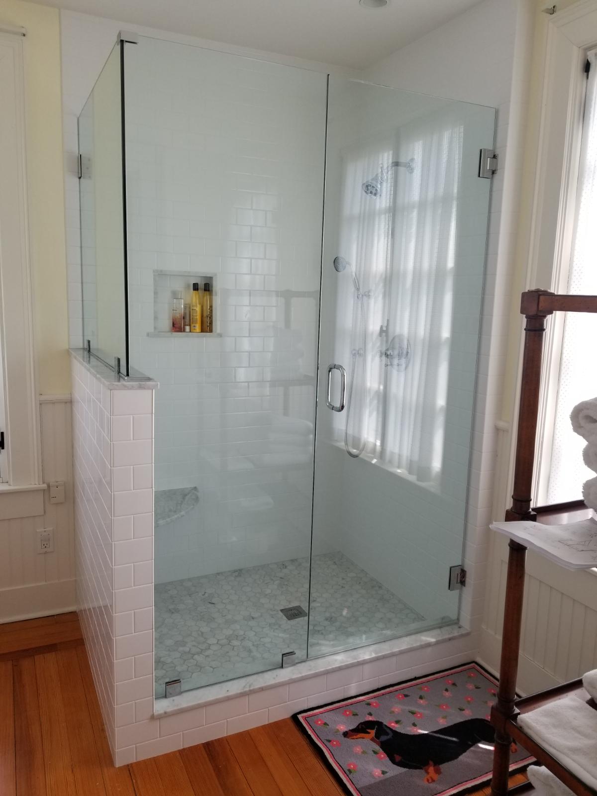 Glass shower with white tile, gray floor, and a dog-themed mat on a hardwood floor.