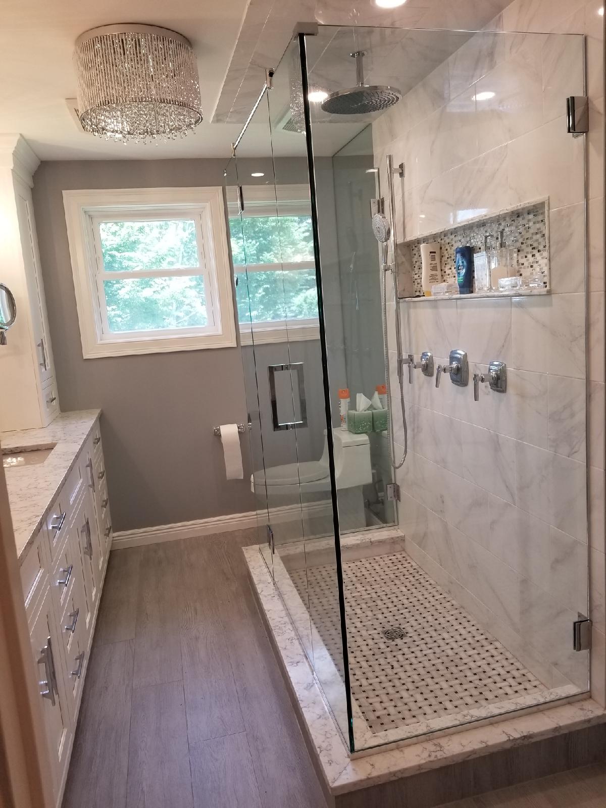 Modern bathroom with walk-in shower, white cabinets, grey walls, and a window.
