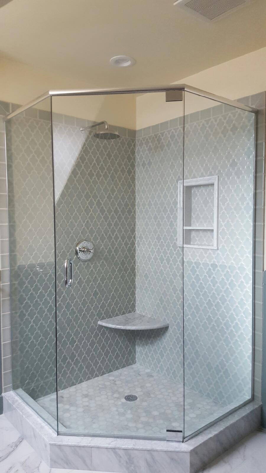 Glass shower with gray patterned tile and a built-in seat.