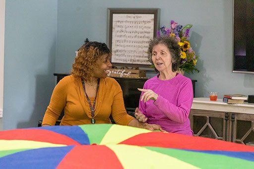 Two women are playing with a colorful parachute in a room.