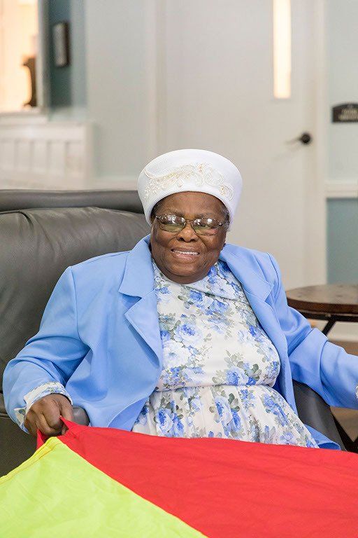 An elderly woman is sitting in a chair holding a parachute.