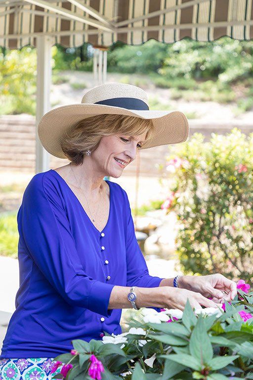 A woman wearing a hat and a blue shirt is looking at flowers.