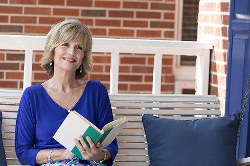 A woman is sitting on a porch swing reading a book.