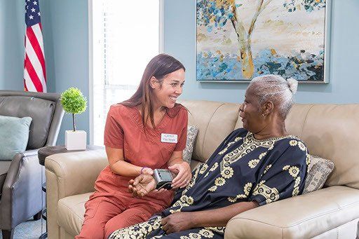 A nurse is talking to an elderly woman sitting on a couch.