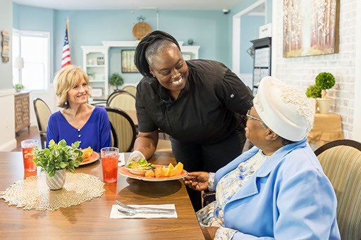 A woman is serving food to two older women at a table.