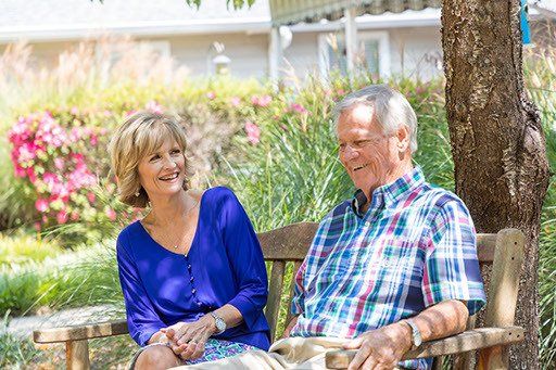 A man and a woman are sitting on a bench under a tree.
