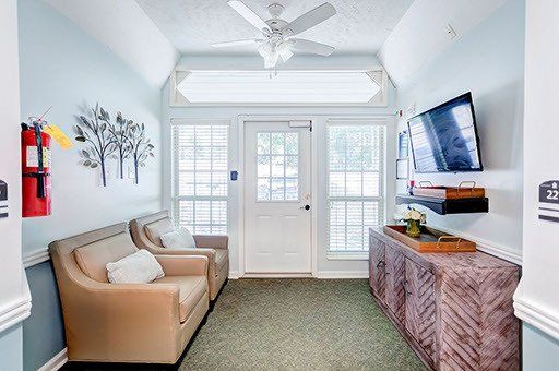 A living room with two chairs , a couch , a television and a ceiling fan.