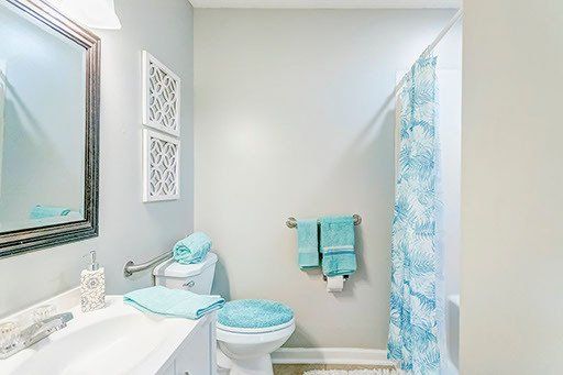 A bathroom with a toilet , sink , mirror and shower curtain.