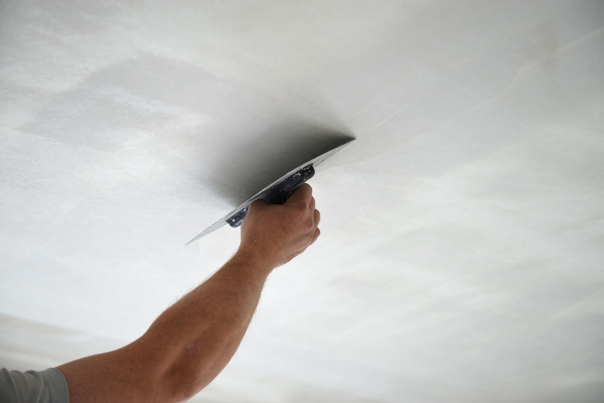 The arm of a master builder renovating a ceiling by using a plastering tool.