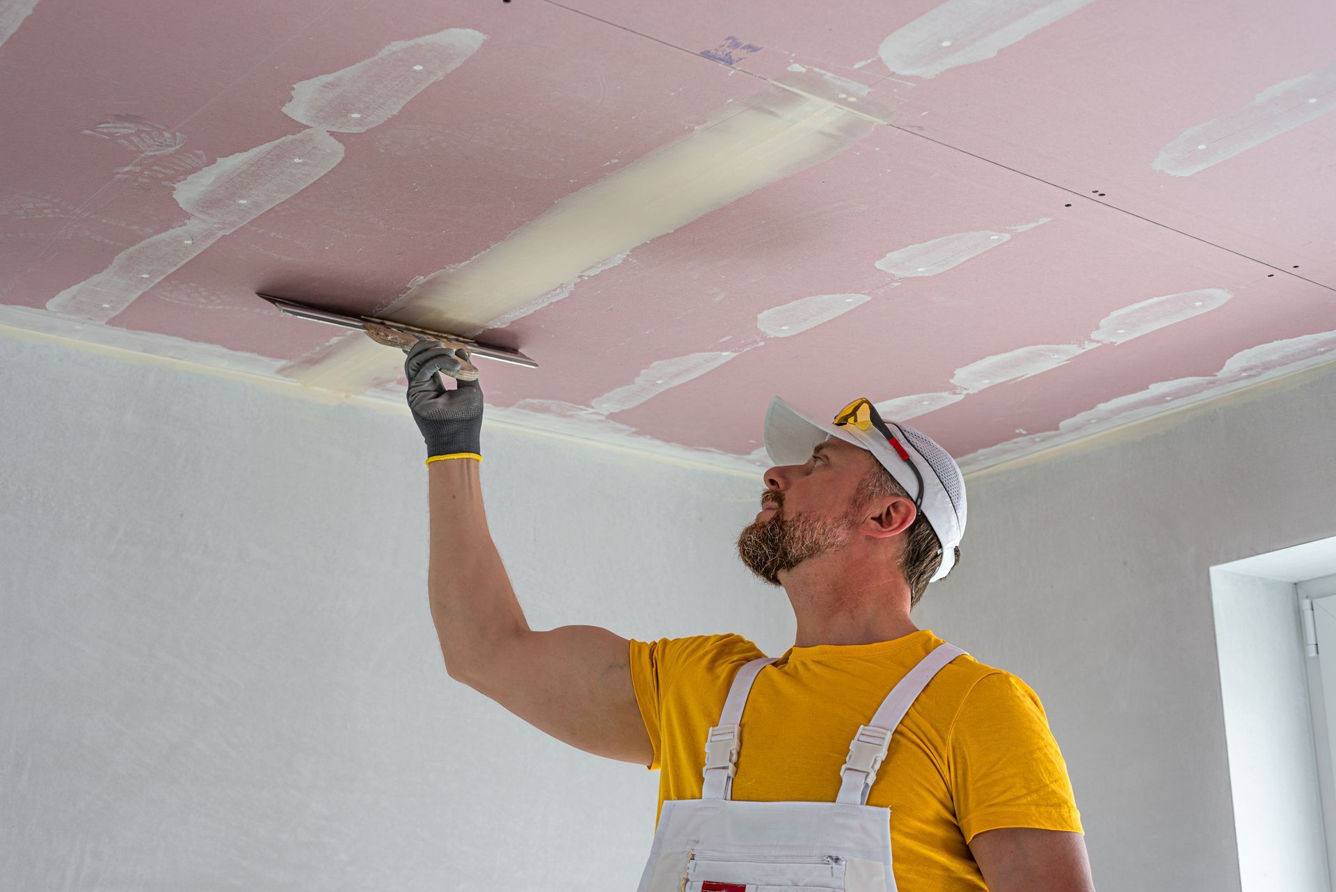 A construction worker is applying plaster to the ceiling using a trowel