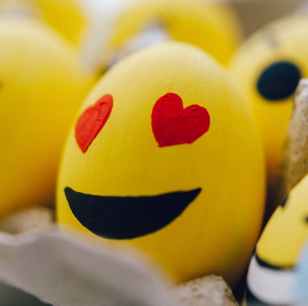 Yellow Easter egg painted with heart eyes and a smile, surrounded by other emoji eggs.