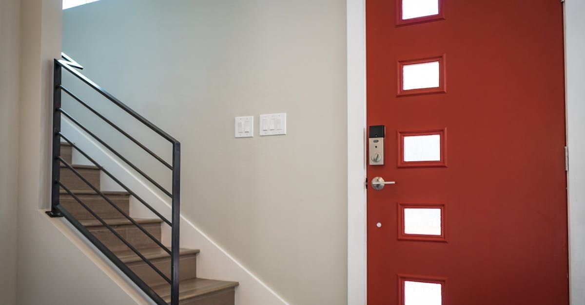 A man in blue overalls is measuring a door in a hallway.