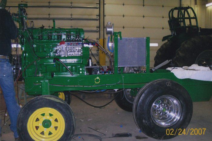 Green and yellow John Deere tractor, modified for pulling competitions, inside a garage.