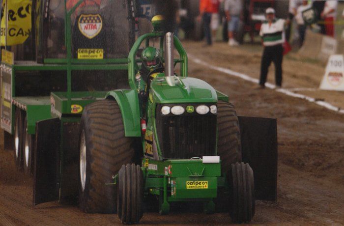Green John Deere tractor pulling a weighted sled on a dirt track.
