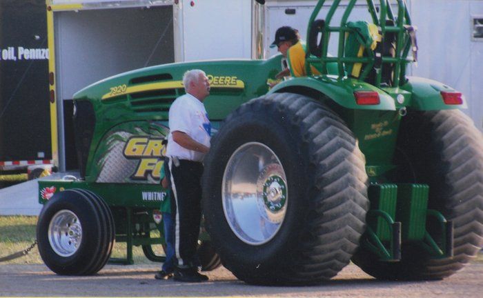 Green and yellow tractor with oversized rear tires; two people stand nearby.